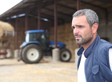 Farmer standing in front of a barn containing a tractor