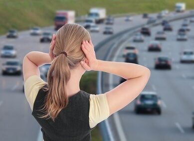 Frau mit Haenden an Ohren vor Autobahn