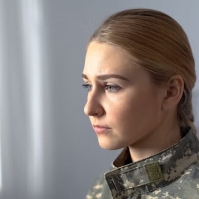 Upset female soldier in military uniform sadly looking in rehab center window
